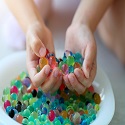 Hydrated water beads in a bowl with a child's hands holding some water beads above the bowl